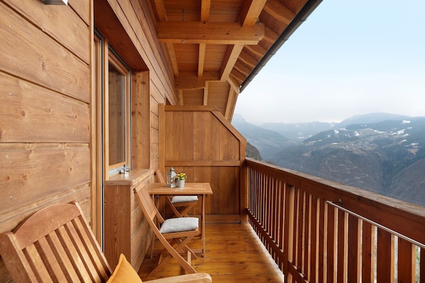 Un balcon en bois, agrémenté d’une table et de chaises, qui offre une vue sur un paysage montagneux.