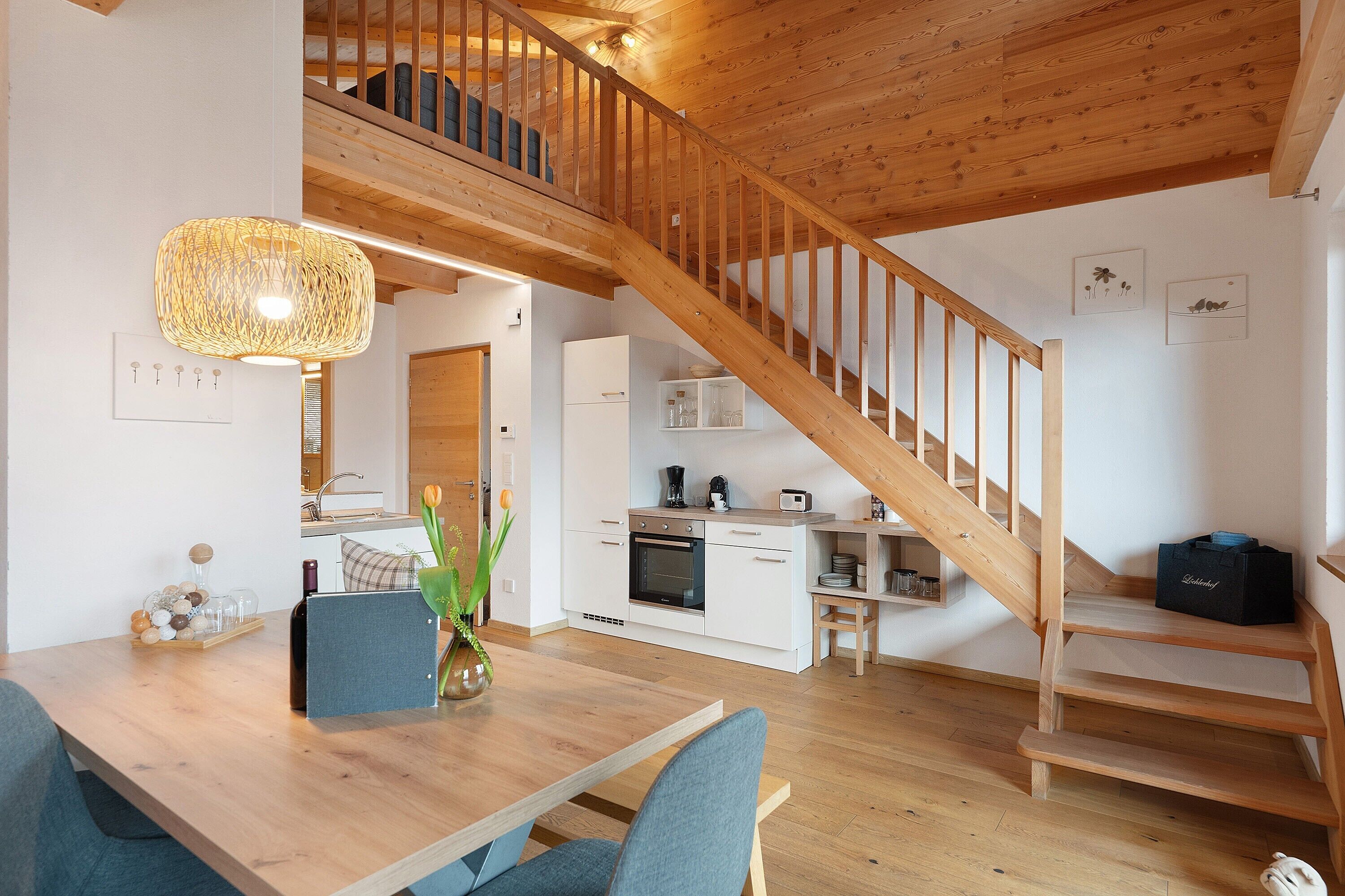 A modern kitchen with white cabinets, a wooden staircase, and a dining area with a table and chairs.