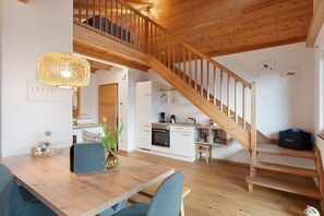 Une cuisine moderne avec des meubles blancs, un escalier en bois et un coin repas comprenant une table et des chaises.