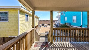 A wooden deck with a view of two beach houses, one yellow and one blue, with a sandy beach and dunes in the background. - AJ: 3 Bedroom Oceanfront Duplex (Carolina Beach)