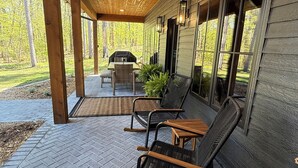 Une terrasse couverte avec un sol en briques, un plafond en bois et une table entourée de chaises.