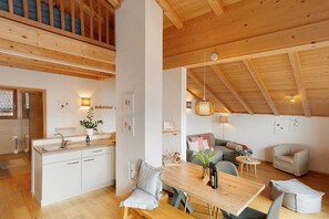 A modern kitchen with white cabinets, a wooden dining table, and a high ceiling with exposed beams.