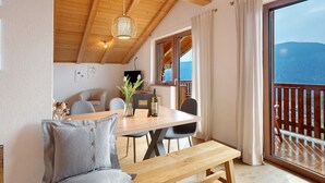 Una mesa de madera con sillas, un banco, una lámpara colgante y vistas a un balcón con barandilla de madera.