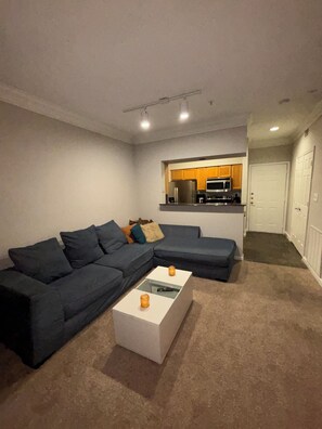 A living room with a sectional sofa, a coffee table, and a kitchenette in the background. - Cozy 1-bedroom apartment in Galleria Houston with pool and gym access (Houston)