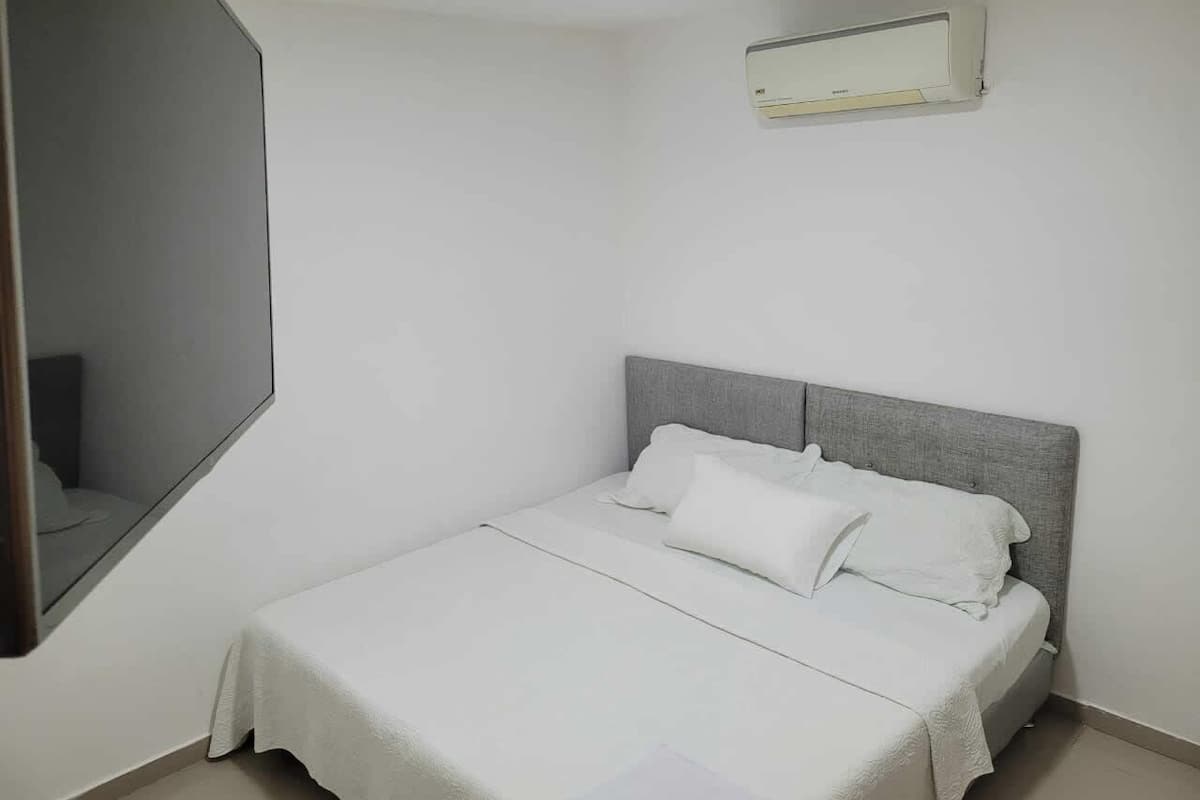 A bedroom with a bed, a bedside table, a mirror, and a wall-mounted air conditioning unit.