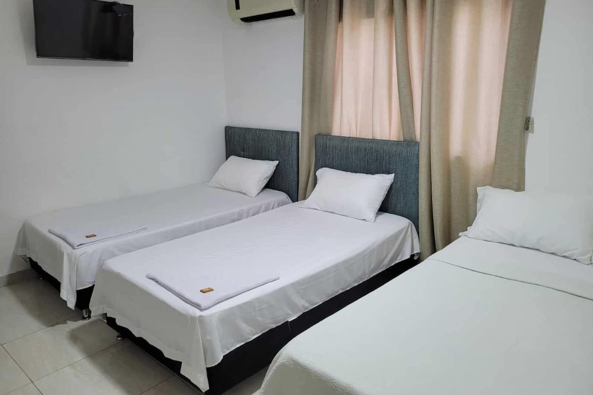 A hotel room with two single beds, a TV mounted on the wall, and an air conditioning unit.