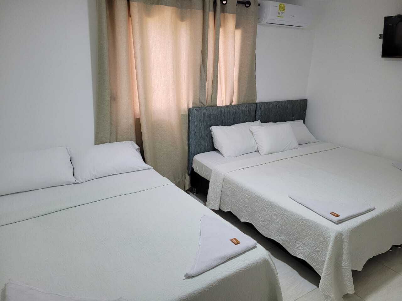 Habitación de hotel con dos camas individuales, cabecera gris, ropa de cama blanca, una cortina y un equipo de aire acondicionado.