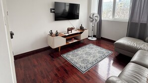 Moderni olohuone, jossa on litteänäyttöinen televisio, valkoinen mediakeskus, lattiavalaisin, kuviollinen matto ja nahkasohva.