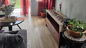 A modern living room with a large window, red curtains, a flat-screen TV, a wooden cabinet, and several potted plants. - House of the Three Companions (Gros Islet)