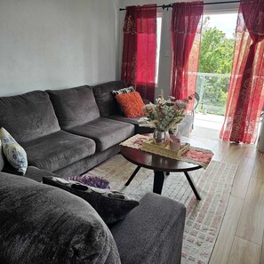 Una sala de estar con un sofá gris, una mesita redonda con un jarrón y una bandeja, y cortinas rojas.