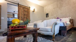 A living room with a wooden coffee table, a white sofa, and a bed with a wooden headboard. - Di Milo Boutique Hotel (Kiwengwa)