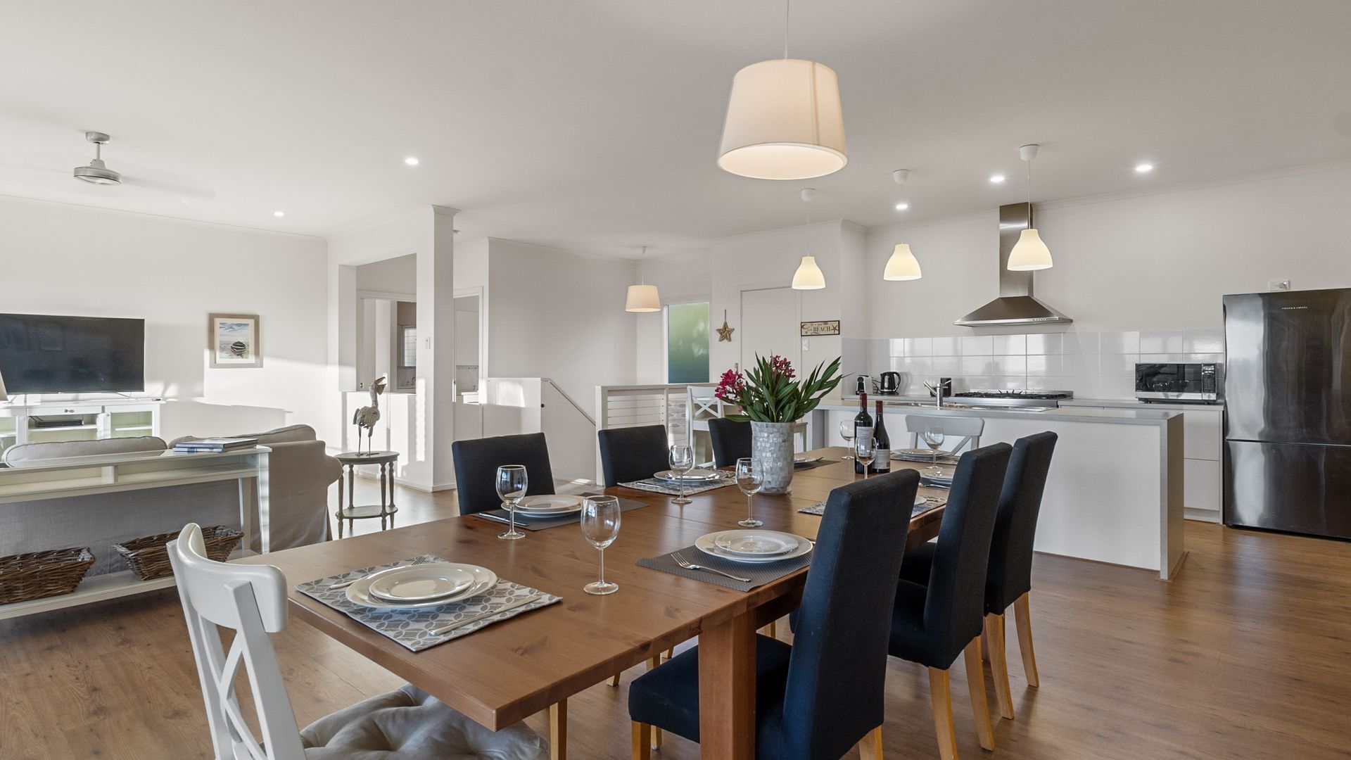 Une cuisine moderne avec un coin repas, comprenant une table en bois pour quatre personnes, un îlot central et des luminaires suspendus.