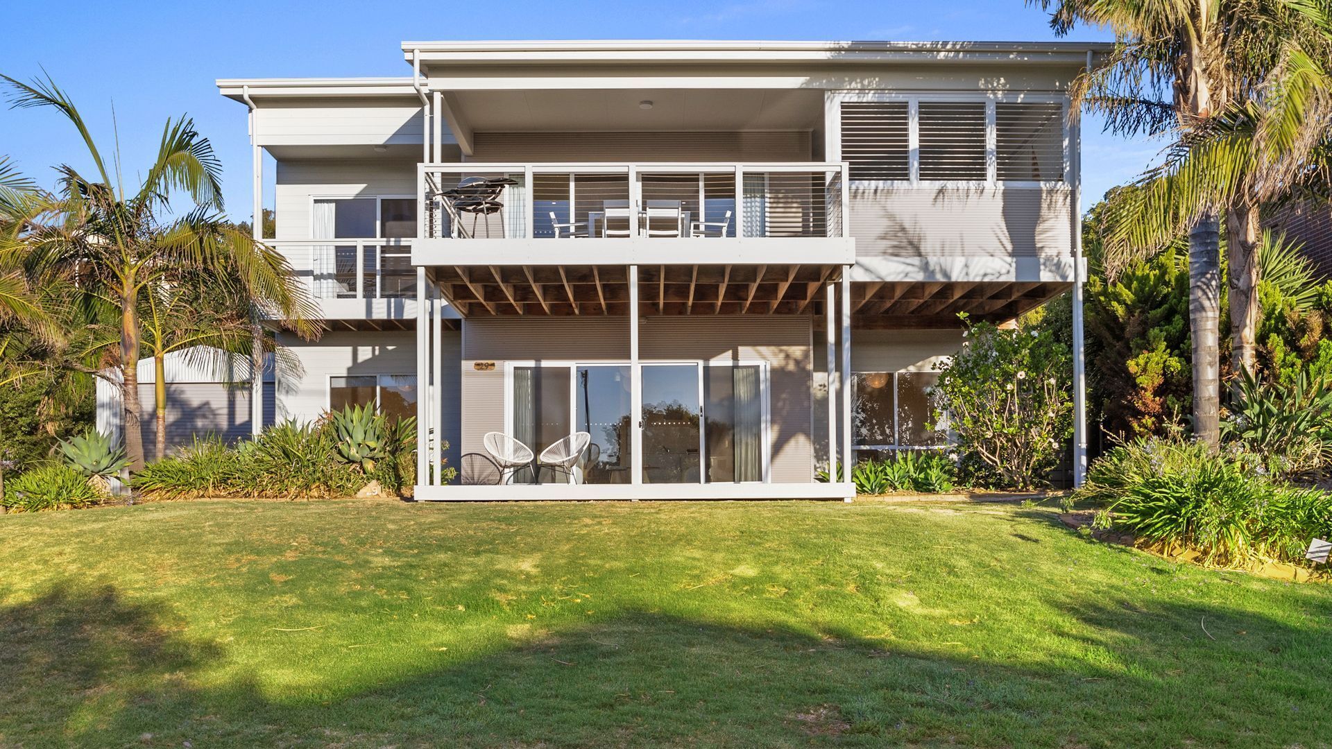 A two-story modern house with a balcony, large windows, and a well-maintained lawn.