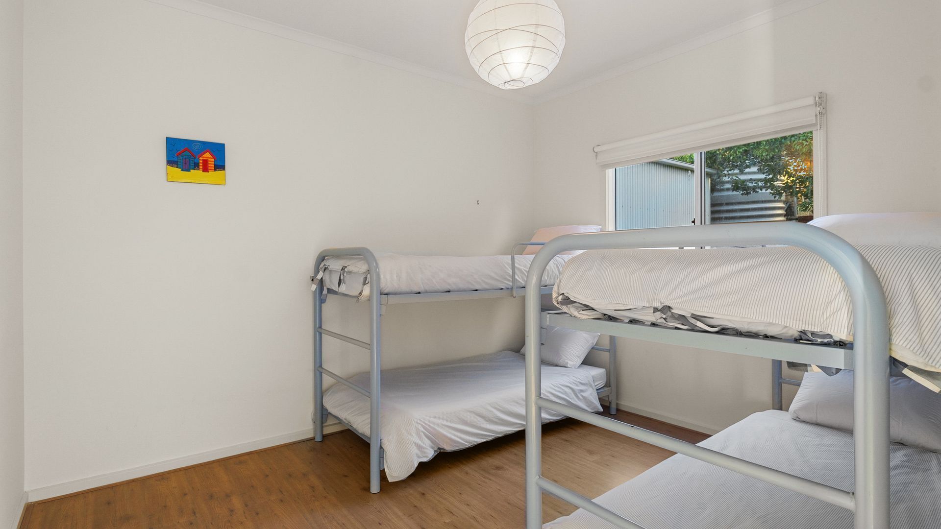 A bunk bed room with a window, a painting on the wall, and a ceiling light.