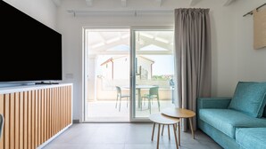 A modern living room with a flat-screen TV, a wooden paneling wall, a teal sofa, and a sliding glass door leading to an outdoor area. - Holiday Home 'Borgo Myricae - Calendula' with Sea View, Wi-Fi and Air Conditioning (Chia)