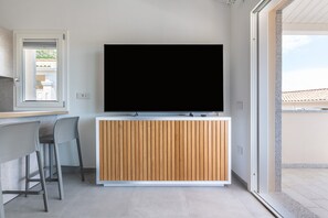 Un salon moderne doté d’un téléviseur à écran plat, de lambris en bois, d’un coin repas avec des chaises et d’une porte-fenêtre coulissante donnant sur un espace extérieur.