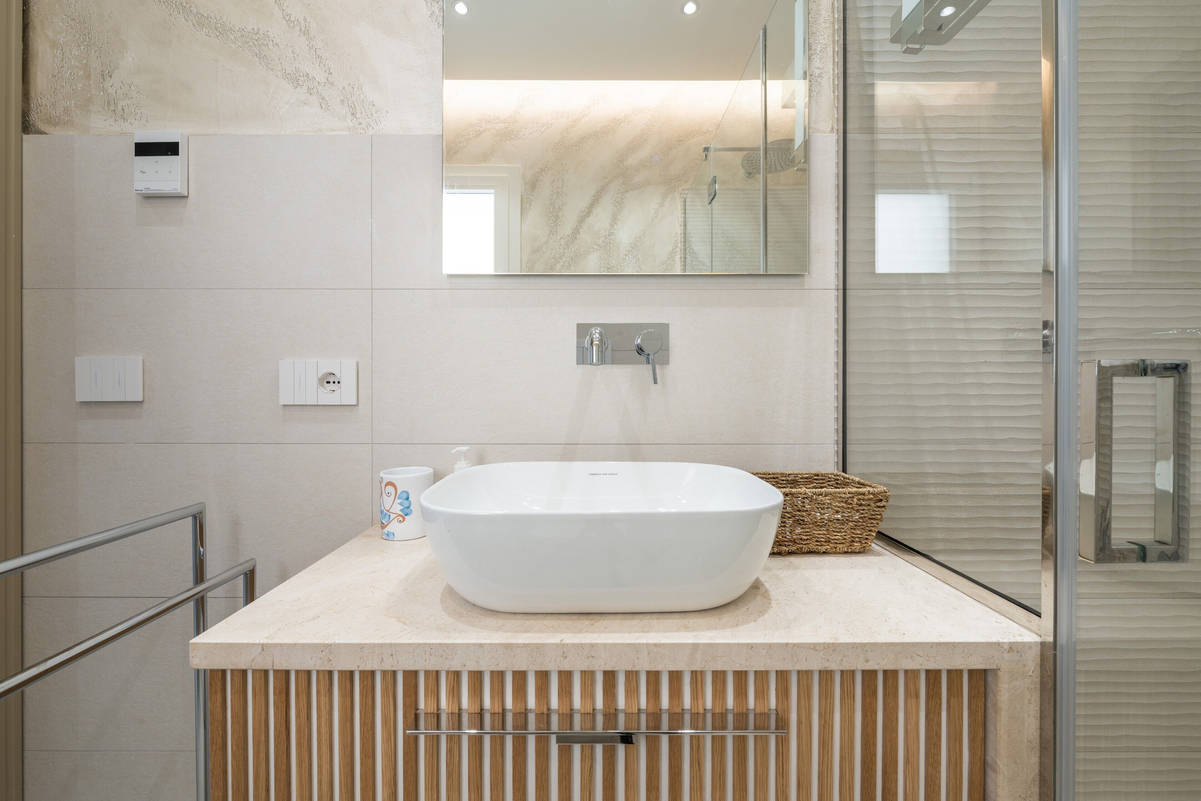 A bathroom with a large white vessel sink, a mirror above it, and a shower area to the right.