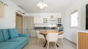 A modern kitchen with white cabinets, a dining table with chairs, and a blue sofa. - Holiday Home 'Borgo Myricae - Scilla Bianca' with Shared Pool, Wi-Fi and Air Conditioning (Chia)