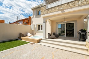 A modern house with a stone facade, a hot tub, and a patio with steps leading to a covered area. - Holiday Home 'Borgo Myricae - Scilla Bianca' with Shared Pool, Wi-Fi and Air Conditioning (Chia)