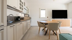 A modern kitchen with a dining area, a flat-screen TV, and a window. - Holiday Home 'Borgo Myricae - Scilla Bianca' with Shared Pool, Wi-Fi and Air Conditioning (Chia)