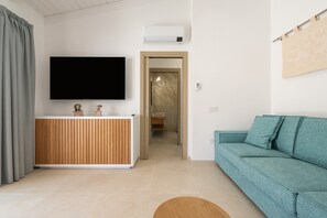 A modern living room with a flat-screen TV, wooden cabinet, teal sofa, and a small round rug. - Holiday Home 'Borgo Myricae - Viola Ciocca' with Mountain View, Wi-Fi and Air Conditioning (Chia)