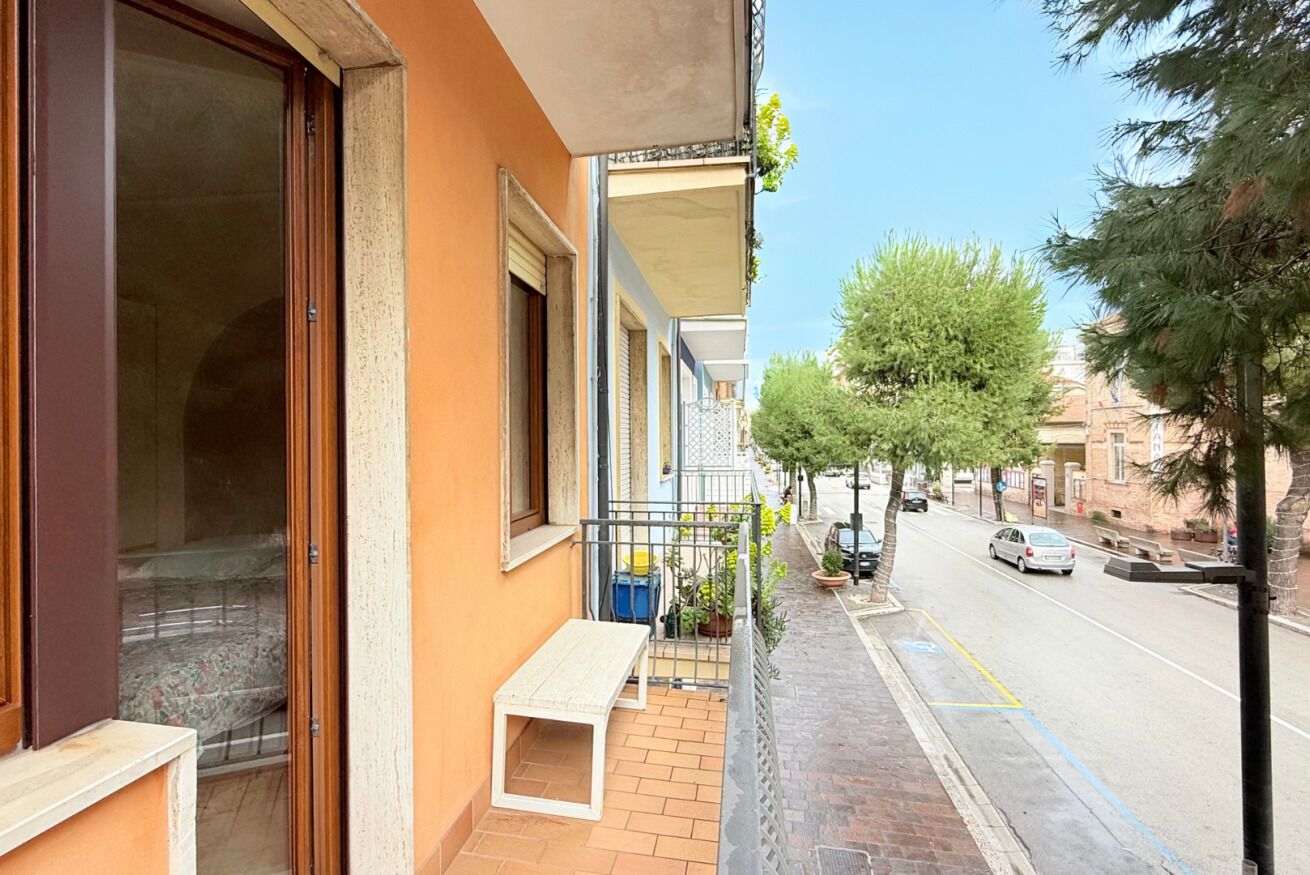 A balcony with a bench, a street view with cars, and trees.