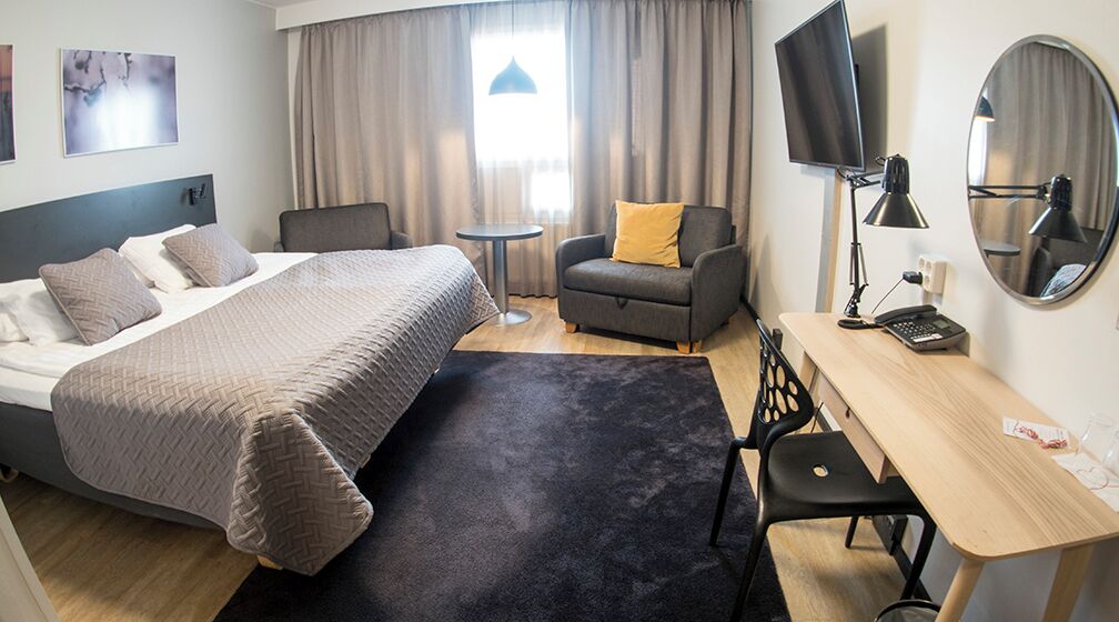 A hotel room with a bed, a desk, a chair, a TV, and a mirror.