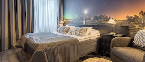 A hotel room with a bed, nightstand, lamp, chair, and a mural of a night sky.