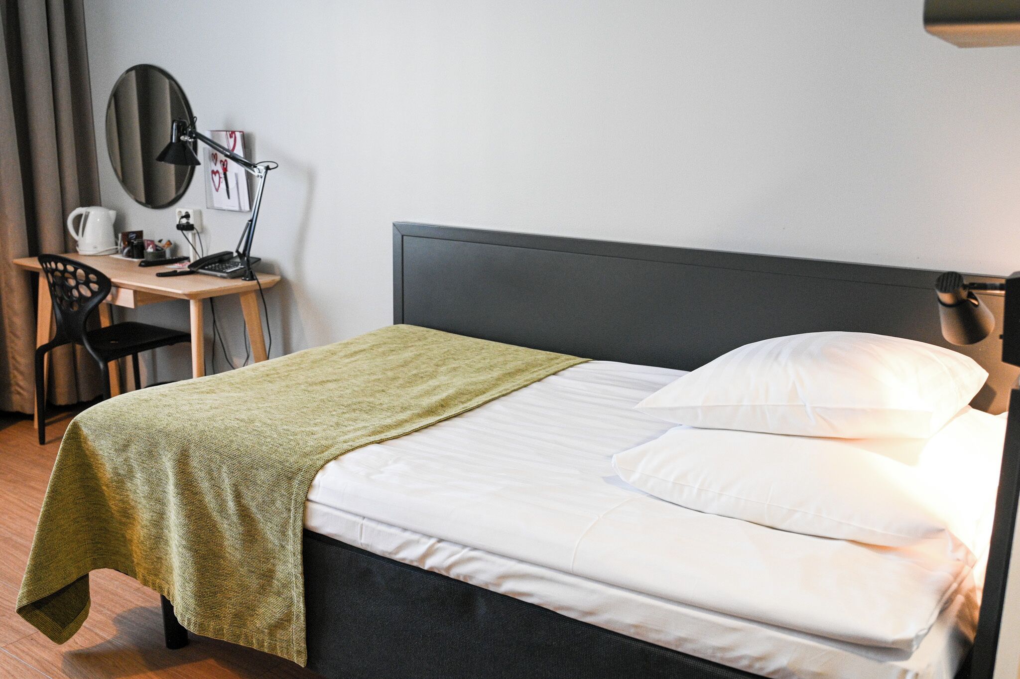 Un letto rifatto con una coperta verde, una scrivania con una lampada e una sedia.