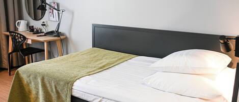 Un letto rifatto con una coperta verde, una scrivania con una lampada e una sedia.