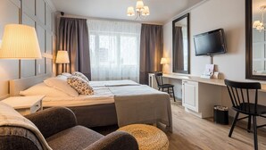 Habitación de hotel con cama, dos mesitas de noche, escritorio con silla, televisor y ventana con cortinas.