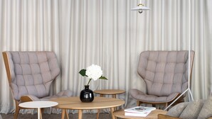 Una sala moderna con dos sillones, una mesa redonda de madera, una lámpara de pie y una pequeña mesa redonda con un florero y un libro.