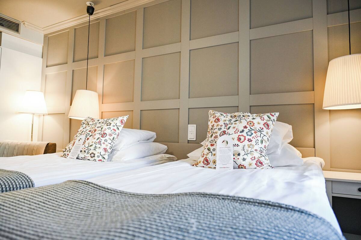 Una camera d'albergo con un letto grande, due lampade ai comodini, una testiera con decorazioni a pannello e un comodino con lampada.