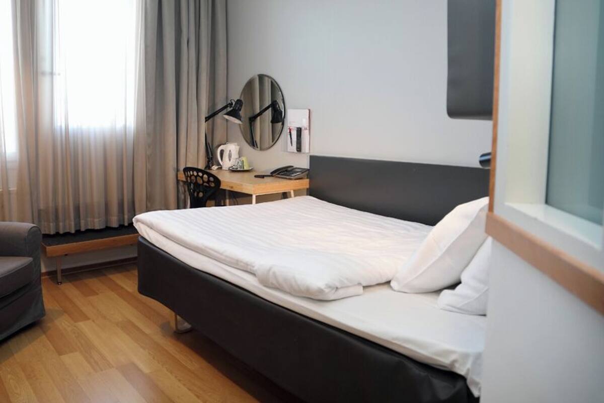 Camera d'albergo con un letto, una scrivania, una sedia, uno specchio e una finestra con tende.