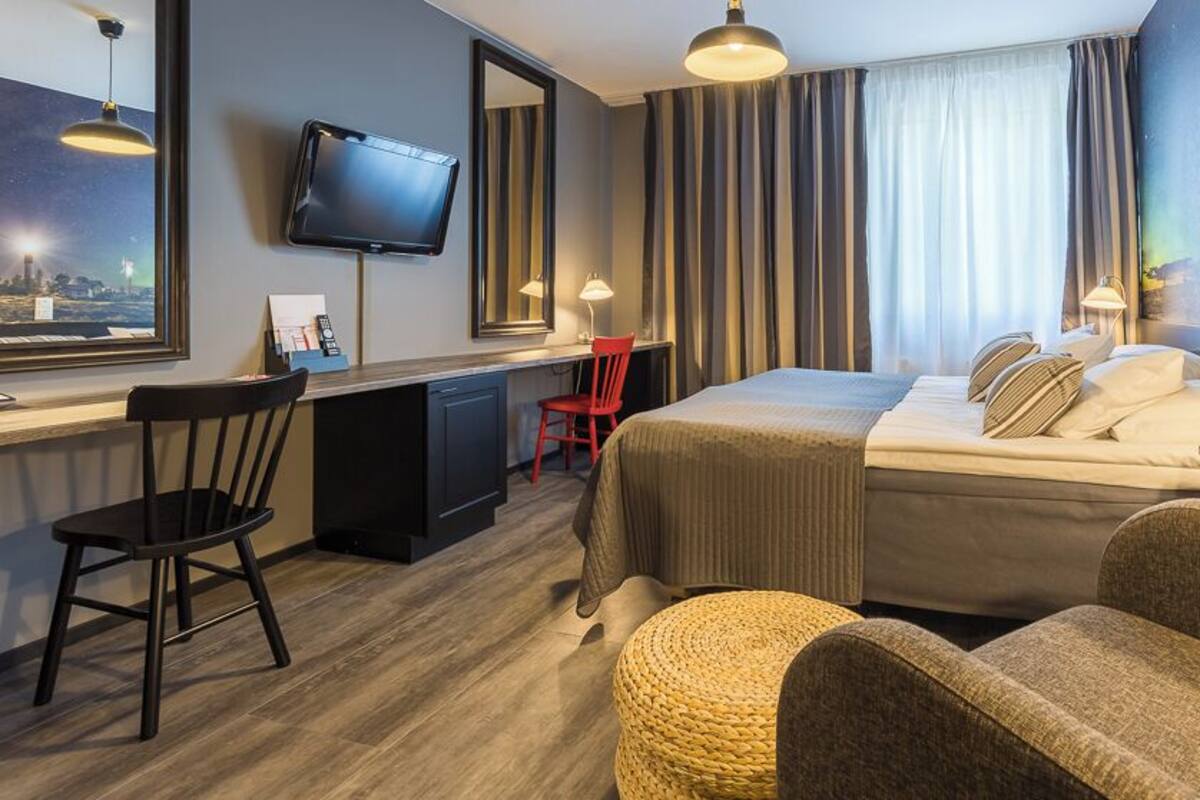 Una camera d'albergo con un letto, una scrivania, una sedia, la televisione e ampie finestre.