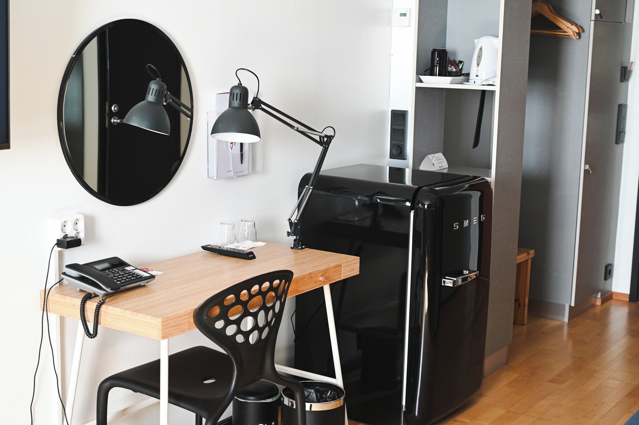 Habitación pequeña con escritorio, silla, refrigerador negro y espejo redondo.