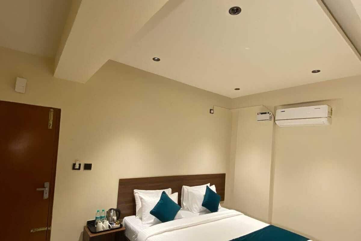 A hotel room with a bed, a nightstand, a door, and an air conditioning unit.