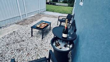 An outdoor patio with a table, chairs, a bottle of champagne, and a cooler filled with bottles.