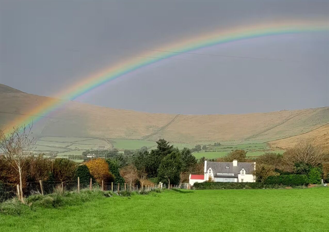 Un paysage rural avec une maison, des champs verdoyants et un arc-en-ciel.