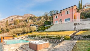 A pool area with a hot tub, stone steps, and a view of a hillside with buildings.