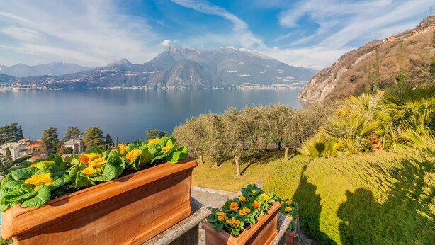 A scenic view of a lake with mountains in the background, a balcony with flower planters, and a clear sky.