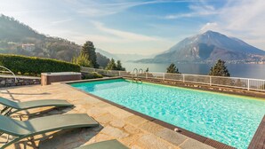 A swimming pool with lounge chairs, a hot tub, and a view of a lake and mountains.