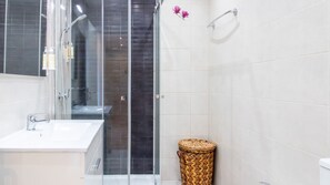 Une salle de bain moderne avec une douche à parois de verre, un lavabo blanc et un panier en osier.