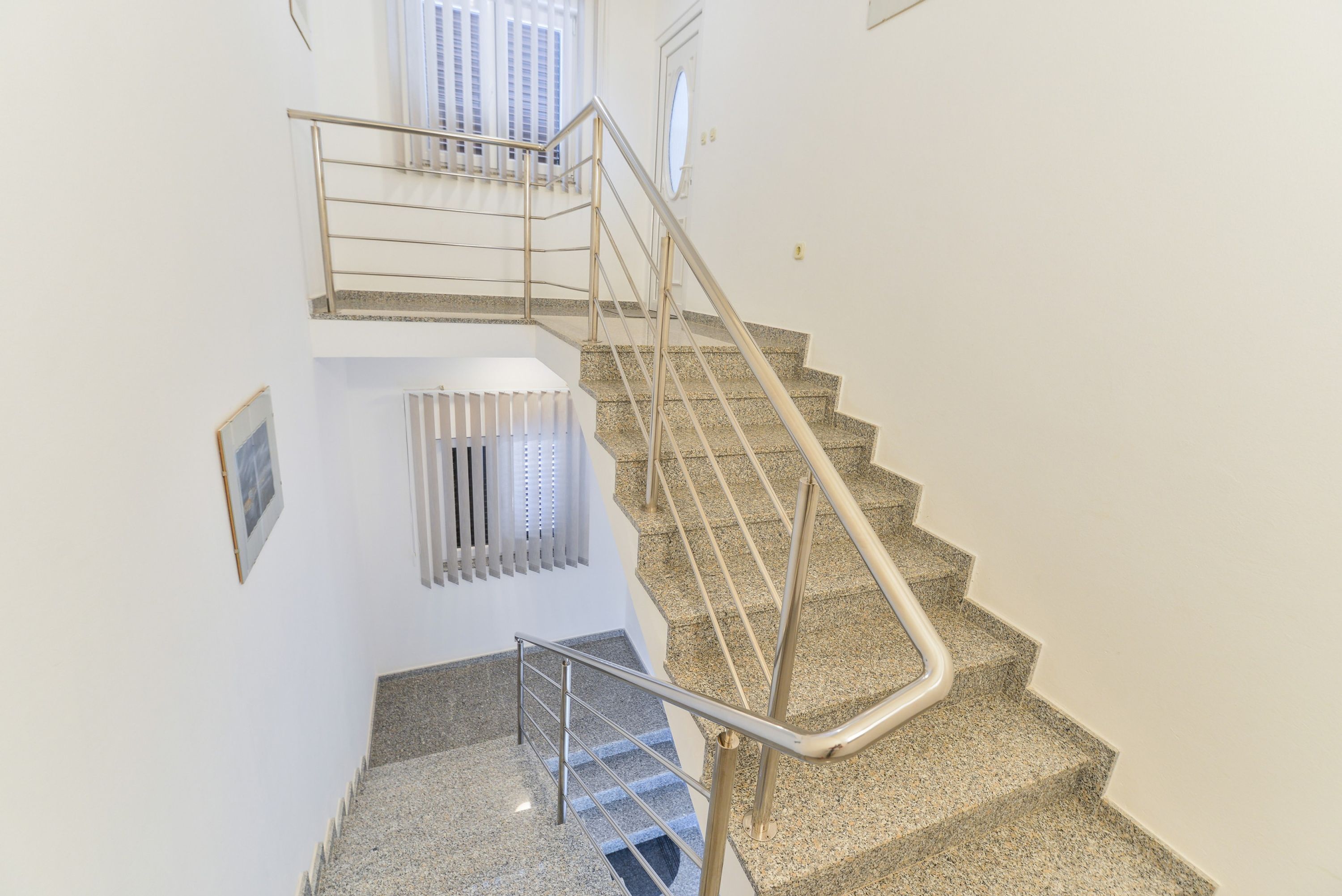 Una escalera con barandillas de metal y peldaños de granito.