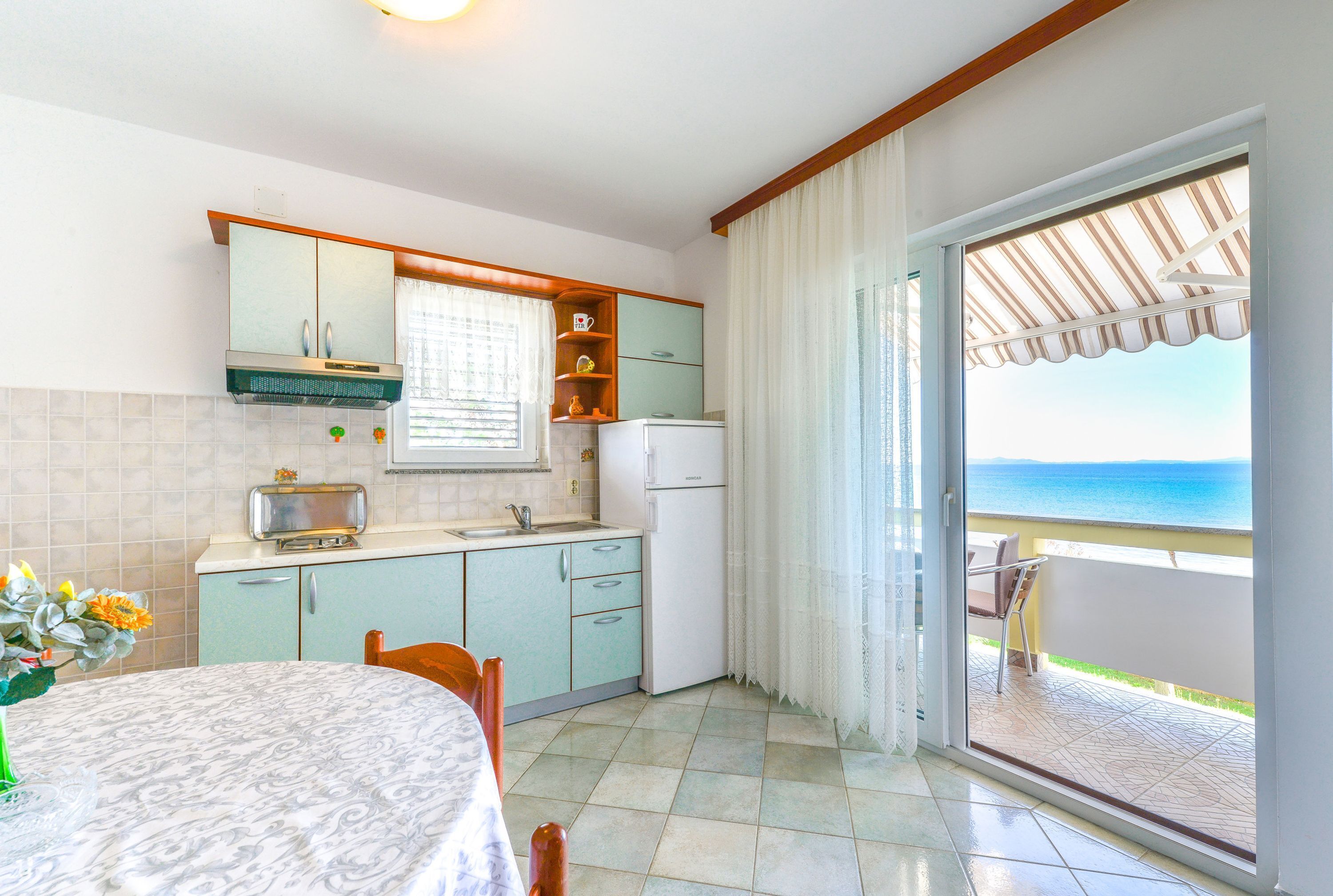 A kitchen with a view of the sea, a dining table, and a balcony with a chair.