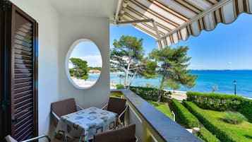 A balcony with a table and chairs, overlooking a pool and the sea.
