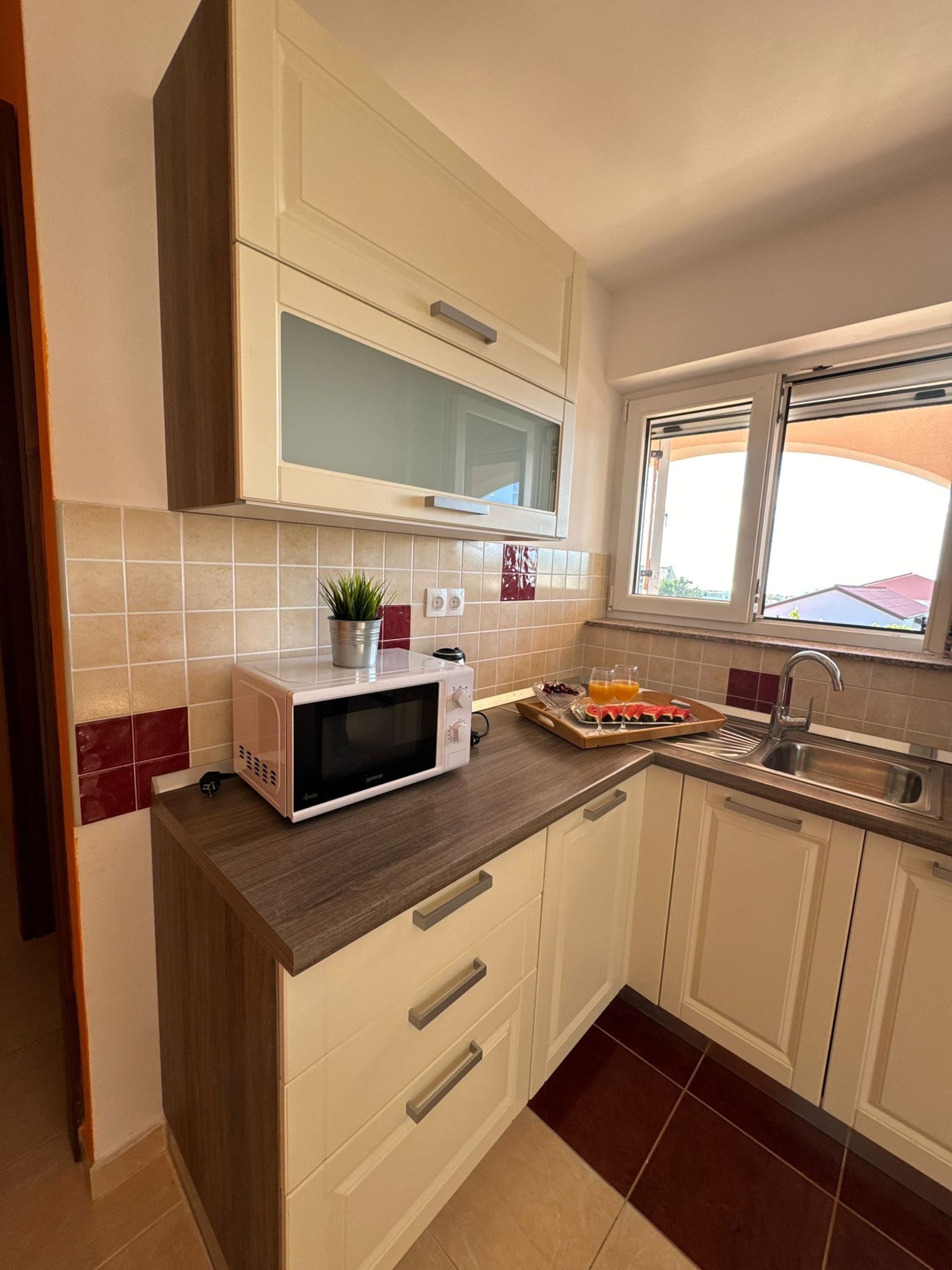 A kitchen with white cabinets, a microwave, a window, and a countertop with a tray of fruit and a plant.