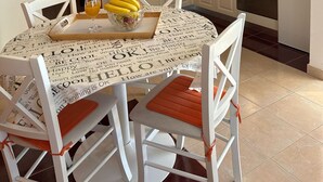 Eine kompakte Küche mit weißen Schränken, einer Mikrowelle und einem Herd. Es gibt einen Esstisch mit Stühlen sowie ein Tablett mit Bananen und einem Glas Orangensaft.
