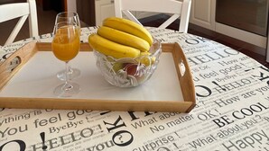 Eine Küche mit weißen Schränken, einer Mikrowelle und einem Fenster. Auf dem Tisch steht eine Schale mit Orangensaft und eine Obstschale.