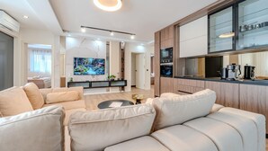 Una sala de estar moderna con un sofá, una mesa de centro y un televisor. Cuenta con una zona de cocina con armarios y un microondas.